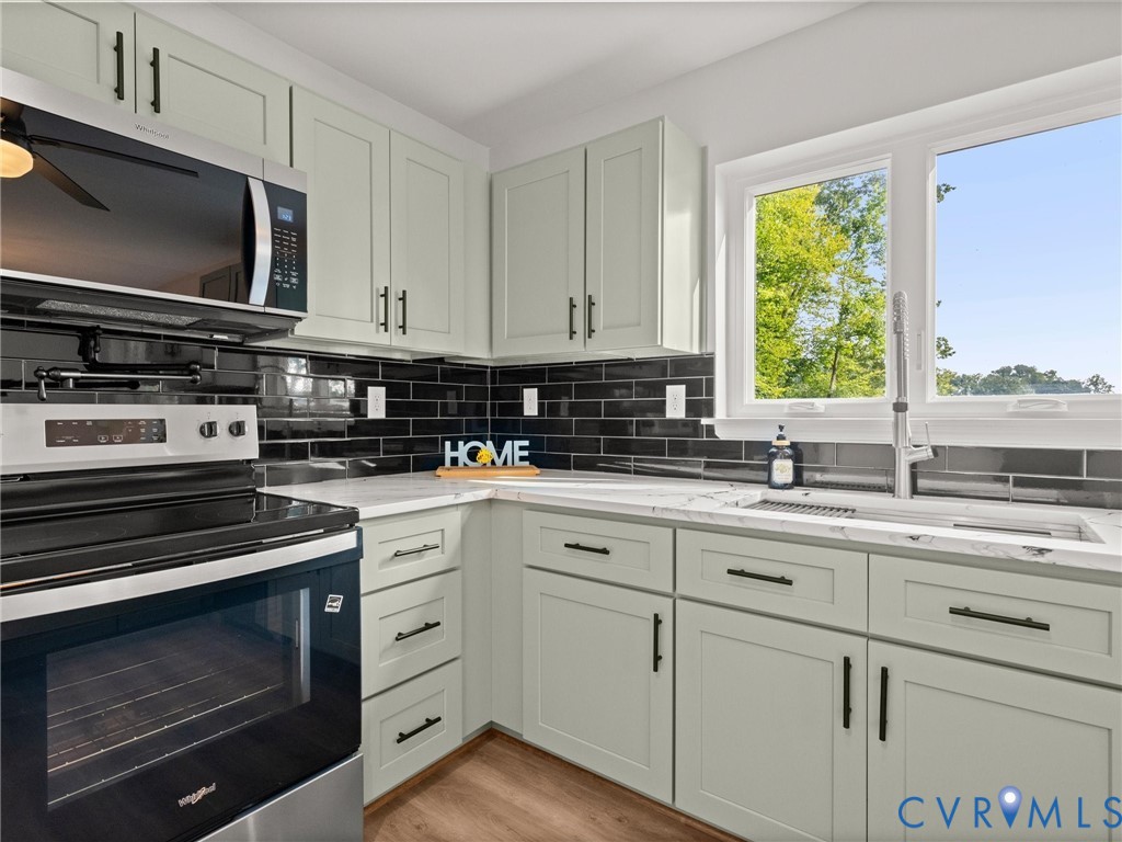 Light-toned cabinetry with matte black hardware, dark subway tile backsplash, white countertops, stainless steel appliances, and a stainless steel sink with a pull-down faucet