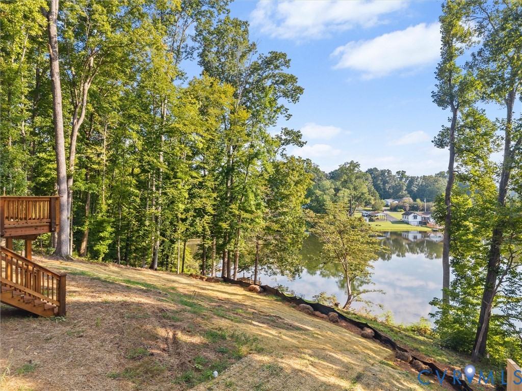 Tiered wood deck with stairs, expansive lawn, mature trees, and waterfront access