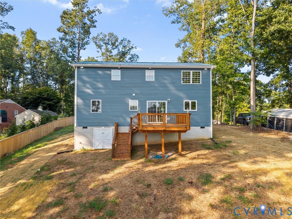 Blue siding exterior with a metal roof, featuring a wooden deck with railing, sliding glass doors, and a ground-level storage door
