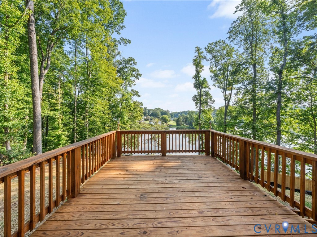 Wood deck with railing overlooking a body of water, surrounded by mature trees