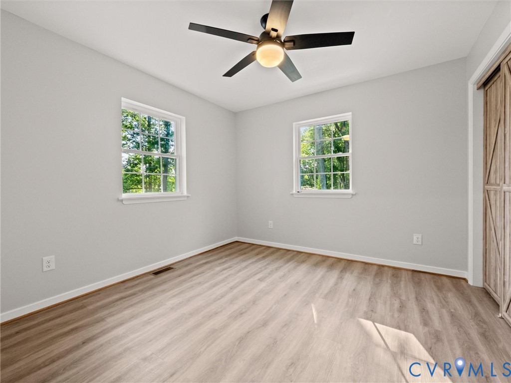 Wood-finish flooring, two windows with white trim, a ceiling fan with integrated lighting, and a wood-finish barn door