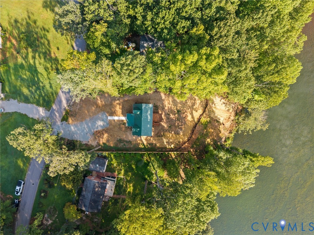 Aerial perspective featuring a property situated at the edge of a body of water, surrounded by mature trees, and accessed by a paved road