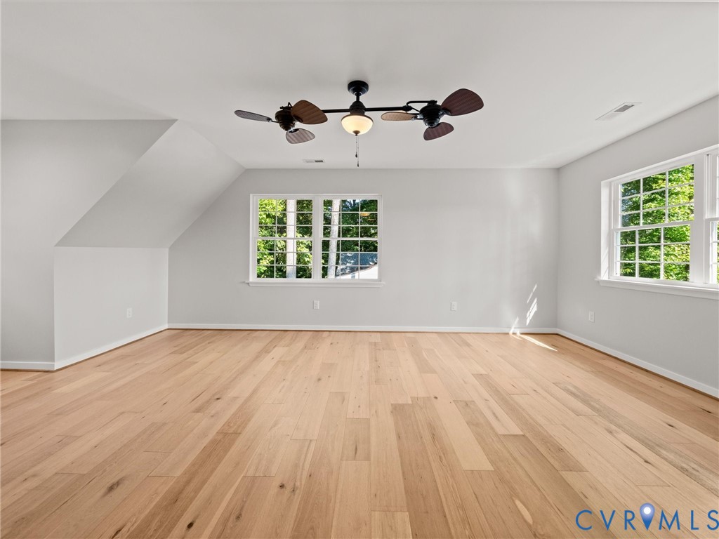 Bright interior space featuring wood-finish flooring, multiple windows, a ceiling fan with integrated lighting, and sloped ceiling details