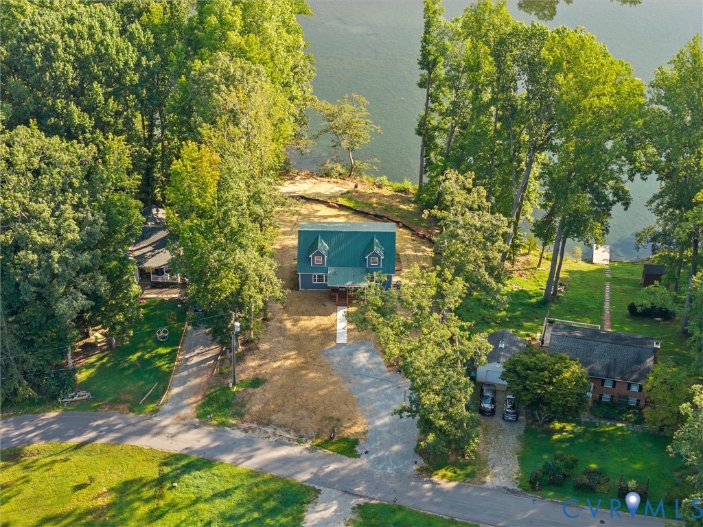 Waterfront property featuring a blue siding exterior, a green metal roof, and surrounding mature trees