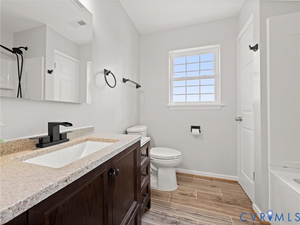 Wood-finish tile flooring, dark wood vanity with ample storage, integrated basin with light-toned countertop, and matte black fixtures