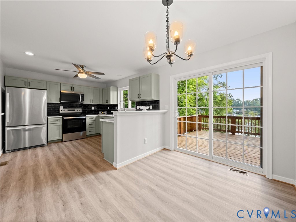 Contemporary kitchen with stainless steel appliances, light green cabinetry, dark tile backsplash, and light wood-finish flooring