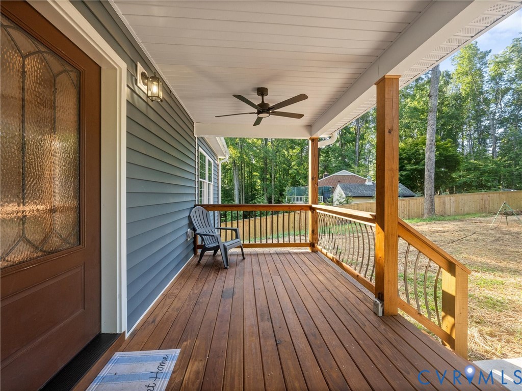 Covered front porch featuring wood-finish decking, dark gray siding, and a decorative glass-paneled entry door