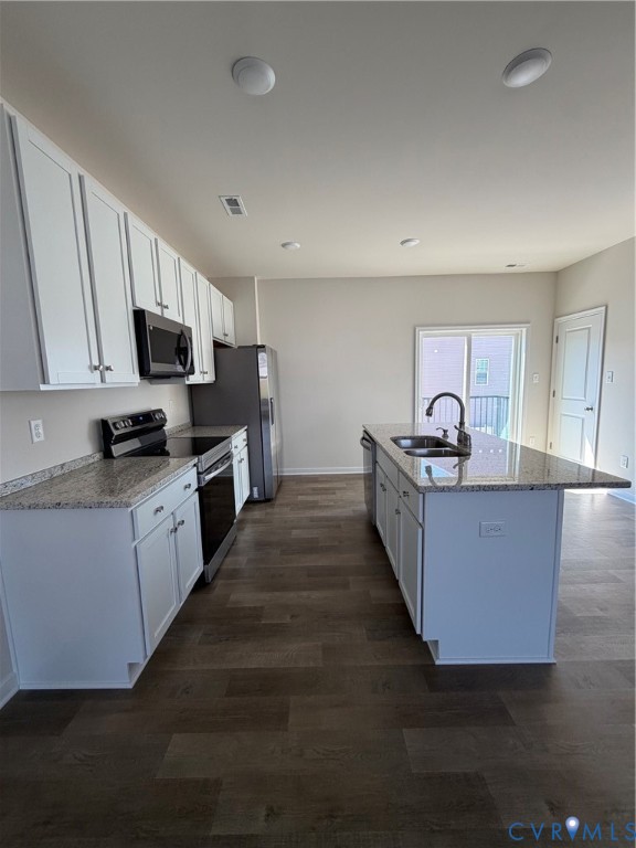 Contemporary kitchen featuring white cabinetry, granite-style countertops, stainless steel appliances, a center island with sink, and wood-finish flooring