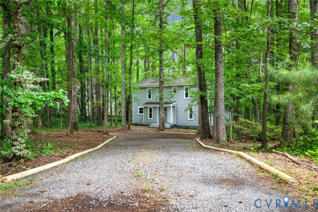 Two-story residence featuring light blue siding, a gravel driveway, and a natural tree-lined setting
