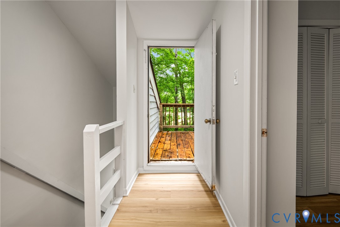 Bright hallway with hardwood flooring and white trim, opening to a spacious deck with wooden decking and lush tree canopy backdrop