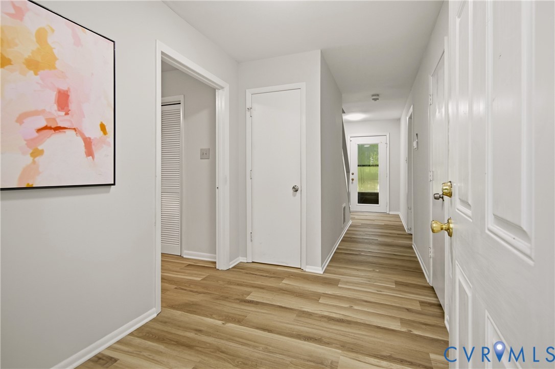 Spacious hallway featuring wood-finish flooring, light grey wall paint, white trim, and multiple white paneled doors