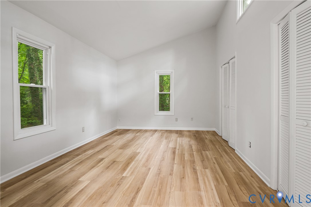 Bright and spacious bedroom featuring gleaming wood-finish flooring, abundant natural light from dual windows, and generous square footage