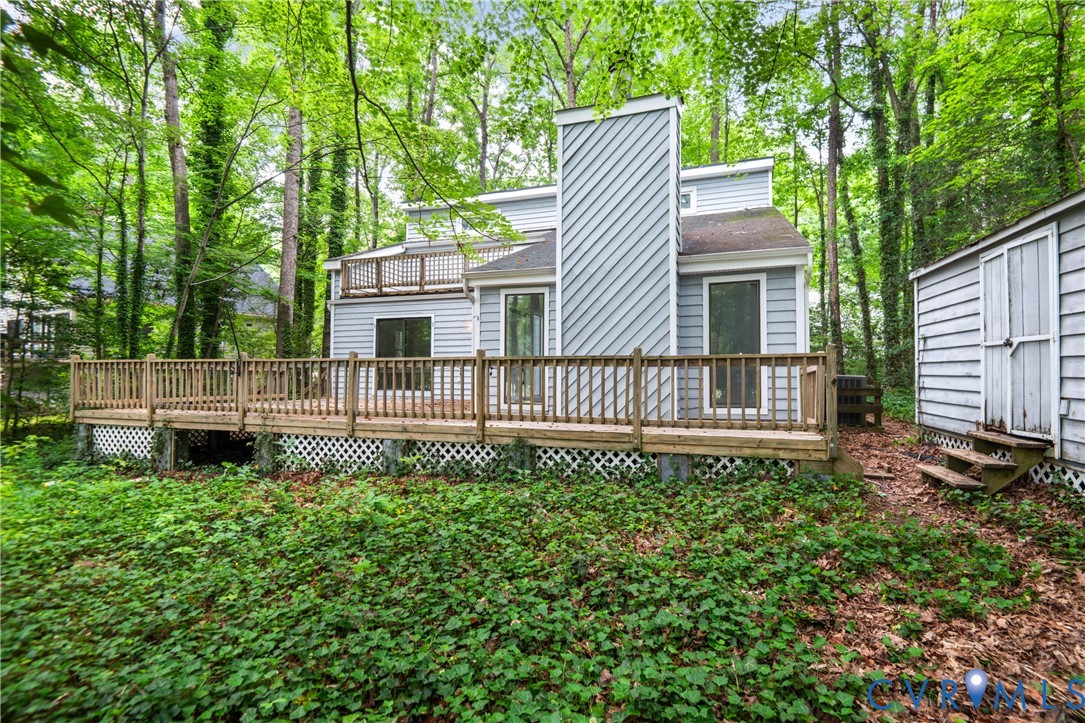 Modern elevated home featuring a striking vertical architectural element and horizontal siding, set on a wooded lot with mature trees