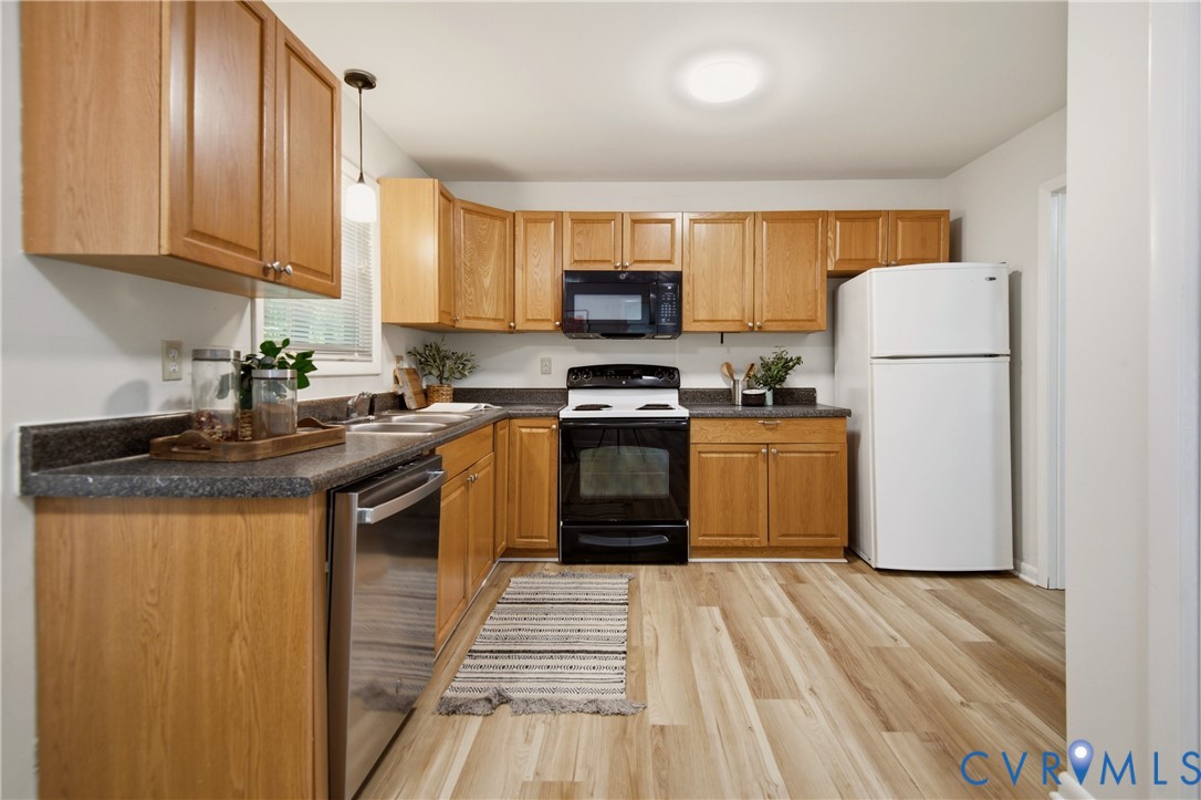 Kitchen featuring wood-finish flooring, light wood cabinetry, dark countertops, a double basin sink, and a stainless steel dishwasher Kitchen featuring wood-finish flooring, light wood cabinetry, dark countertops, a double basin sink, and a stainless steel dishwasher