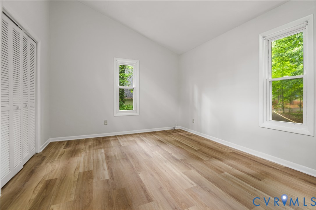 Room with wood-finish flooring, two windows, and a white louvered bifold closet door