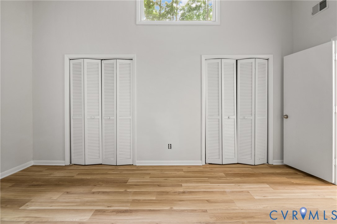 Spacious bedroom featuring gleaming wood-finish flooring, abundant natural light from transom window, and two sets of louvered bifold closet doors providing generous storage solutions