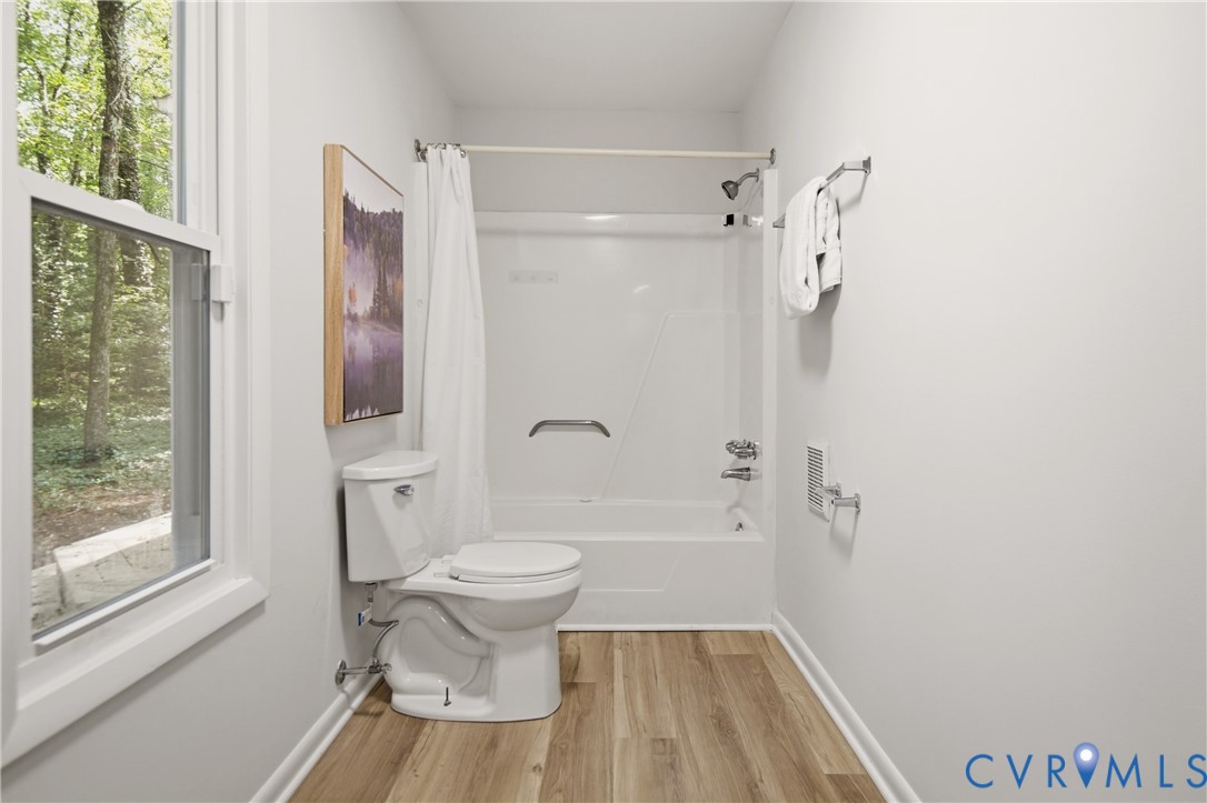 Bathroom featuring wood-finish flooring, a white window frame, a built-in tub and shower combination with a grab bar, and a white toilet