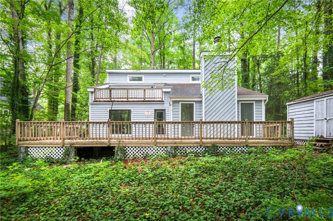 Contemporary home with expansive deck featuring wood railings and lattice detailing, set on a wooded lot with mature trees and natural landscaping