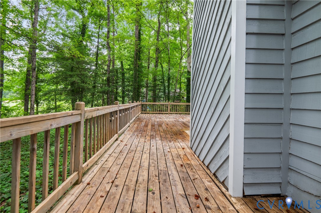 Expansive composite deck featuring rich wood-finish planking, sturdy balusters, and metal railings overlooking mature wooded landscape
