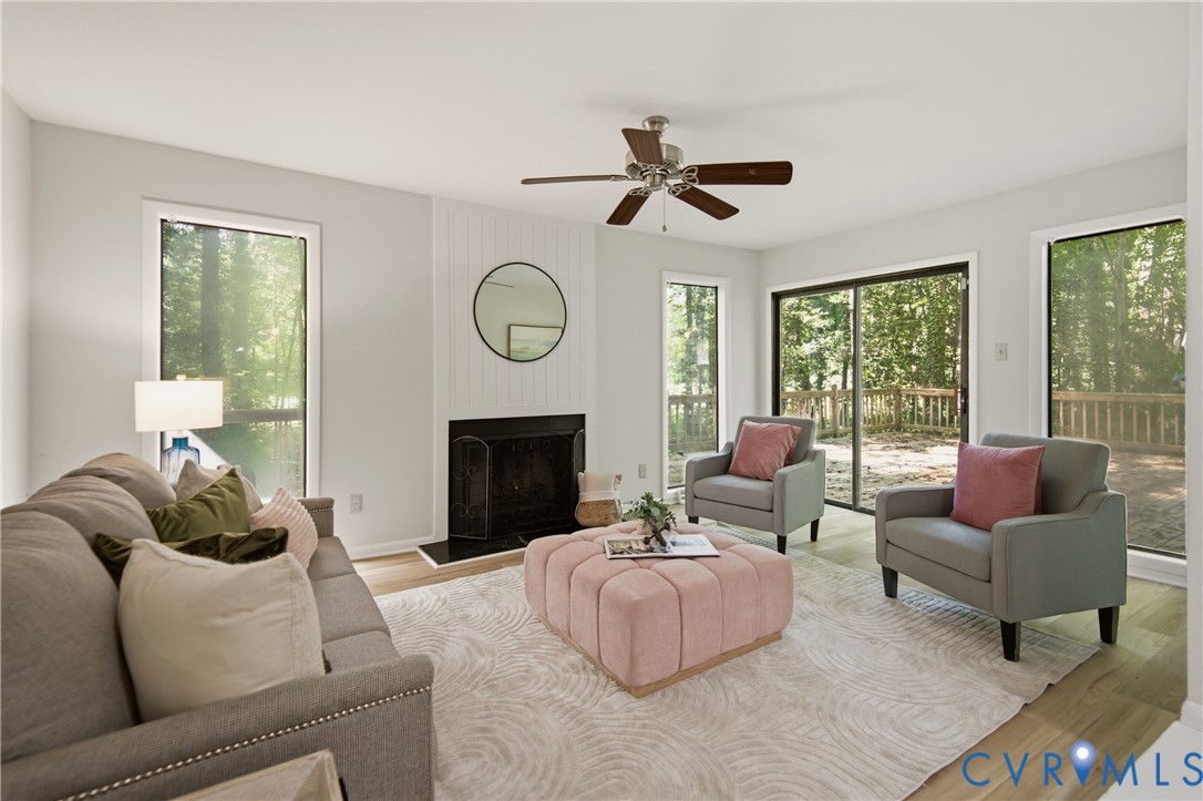 Bright living area featuring wood-finish flooring, a fireplace with a white shiplap-style surround, and a ceiling fan Bright living area featuring wood-finish flooring, a fireplace with a white shiplap-style surround, and a ceiling fan