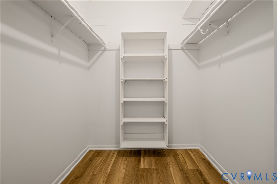 Spacious walk-in closet featuring built-in shelving with five fixed shelves, white painted finishes, and polished chrome hanging rods on both sides