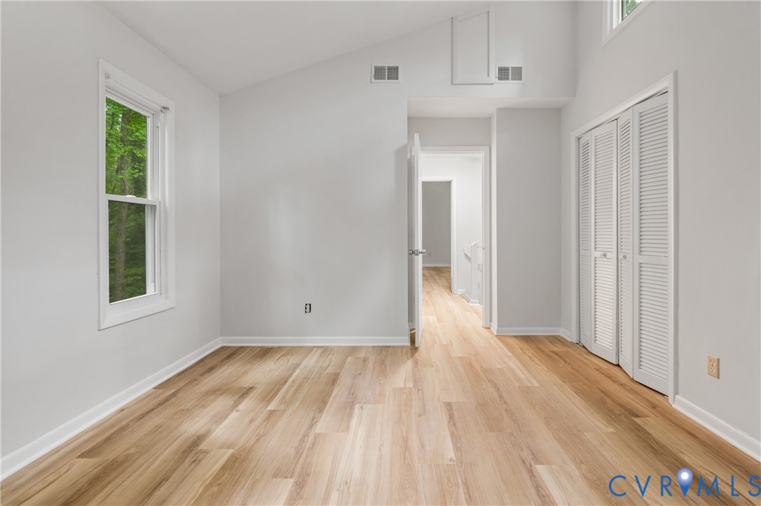 Vaulted ceiling room featuring wood-finish flooring, a double-hung window, white louvered bifold closet doors, and recessed air vents