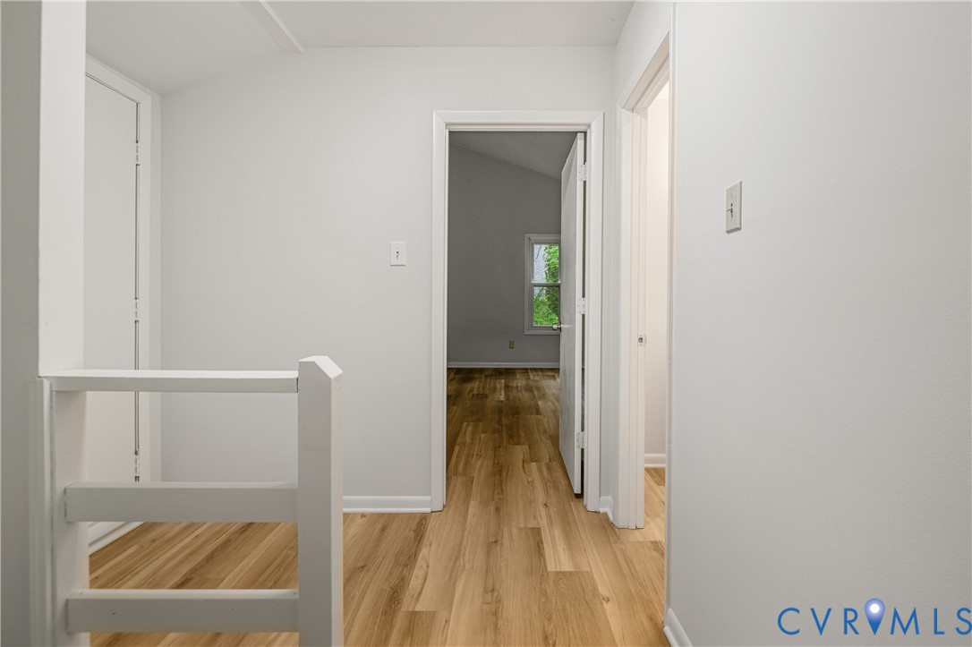 Hallway featuring light wood-finish flooring, white walls, and a white balustrade
