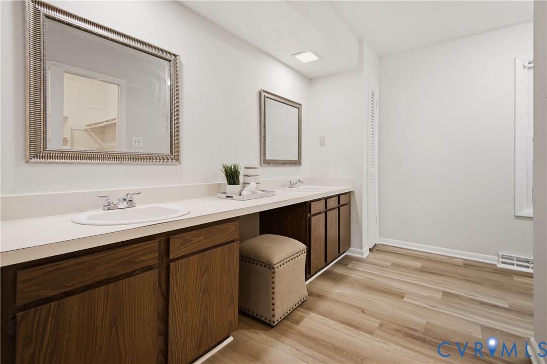 Spa-inspired primary bathroom showcasing dual vanities with white quartz countertops, rich wood cabinetry with decorative hardware, and dual framed mirrors