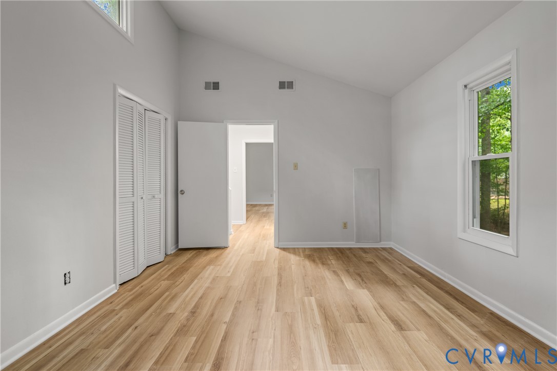 Spacious room featuring wood-finish flooring, vaulted ceilings, and a large window
