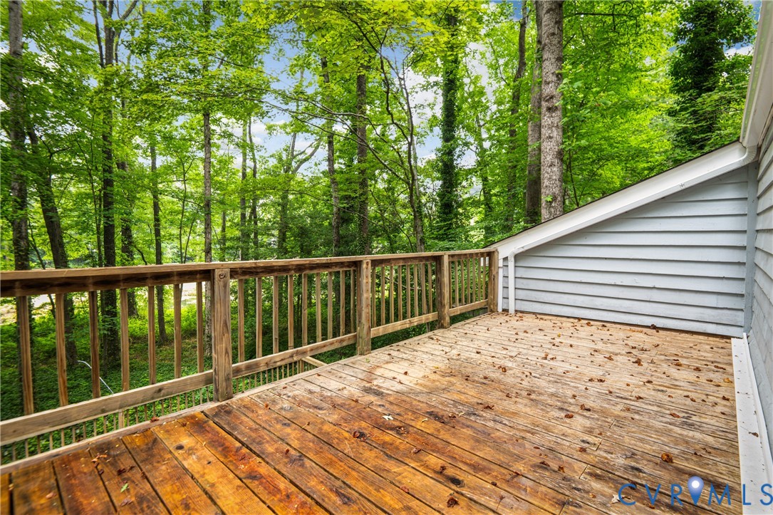 Wood deck with natural wood railing, light blue horizontal siding, and lush green tree canopy