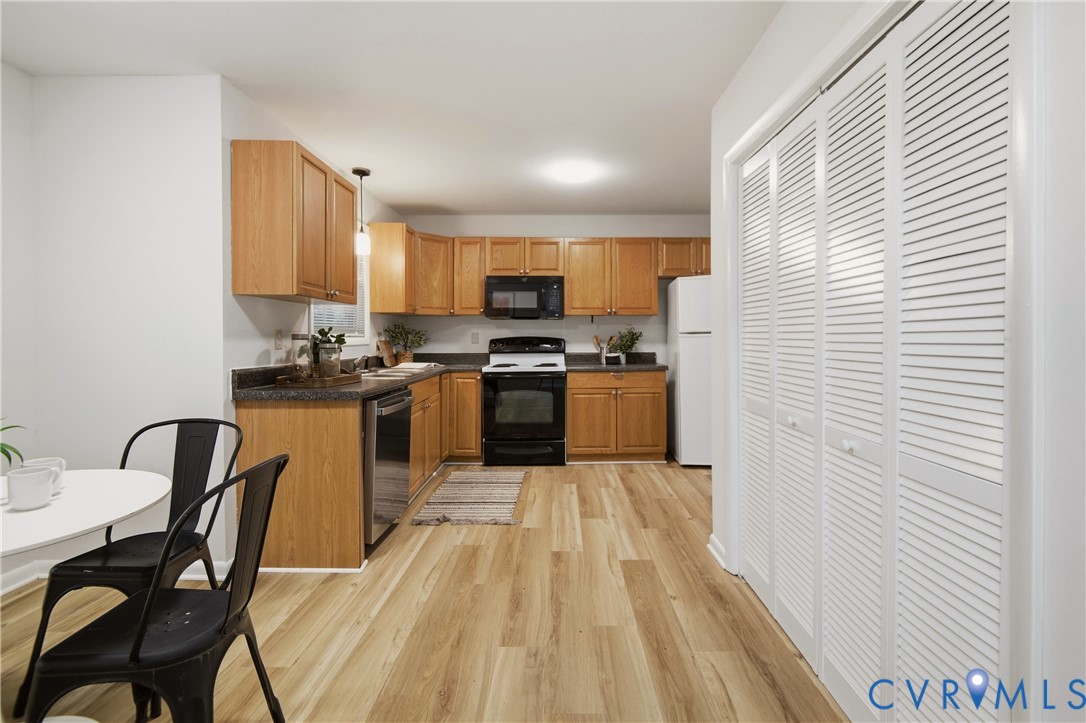 Open-concept kitchen featuring wood-finish flooring, light wood cabinetry, dark countertops, and a full suite of black and stainless steel appliances Open-concept kitchen featuring wood-finish flooring, light wood cabinetry, dark countertops, and a full suite of black and stainless steel appliances