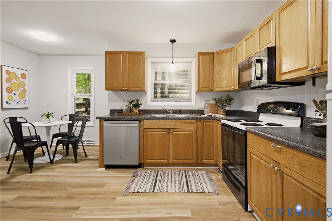 Kitchen featuring wood-finish cabinetry, dark countertops, a stainless-steel dishwasher, and a black range with an overhead microwave