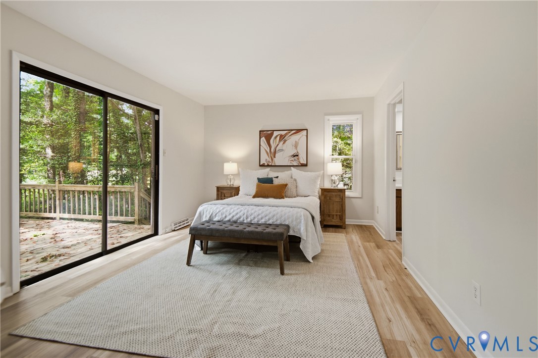 Spacious bedroom featuring wood-finish flooring, a large sliding glass door with exterior deck access, and a secondary window