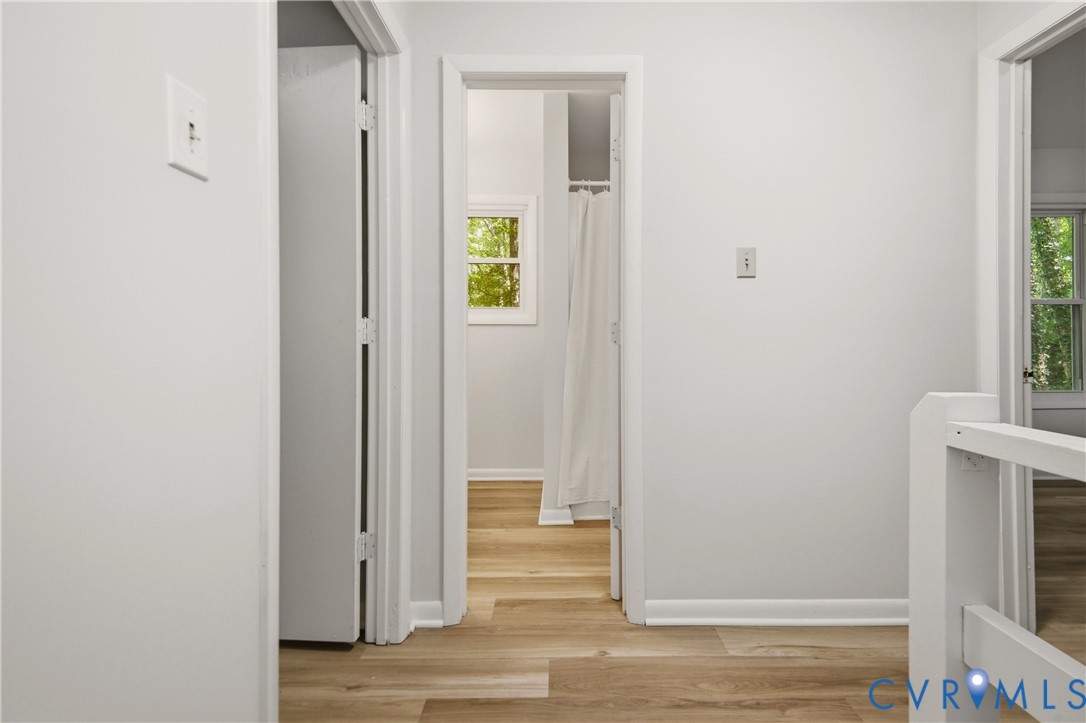 Bright hallway featuring wood-finish flooring, clean white walls, and multiple doorways with white trim