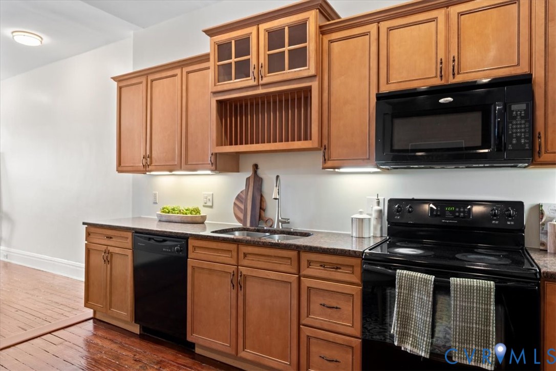 Kitchen featuring wood-finish cabinetry, dark countertops, a built-in microwave, and a black range