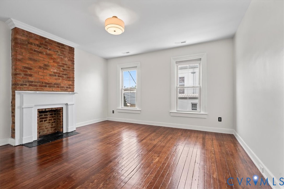 Exposed brick accent wall with a white mantel, hardwood flooring, and two double-hung windows