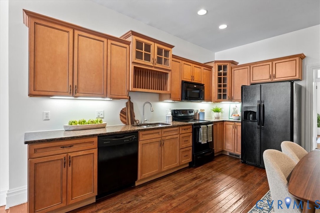 Kitchen featuring wood-finish cabinetry, black appliances, granite countertops, and wood-finish flooring