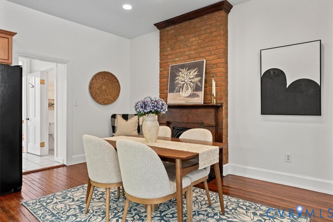 Exposed brick accent wall, wood-finish flooring, white walls, recessed ceiling lighting, and a dark wood mantel