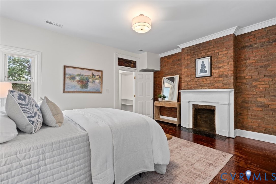 Exposed brick wall, hardwood flooring, white crown molding, a built-in fireplace with a white mantel, and a window with white trim