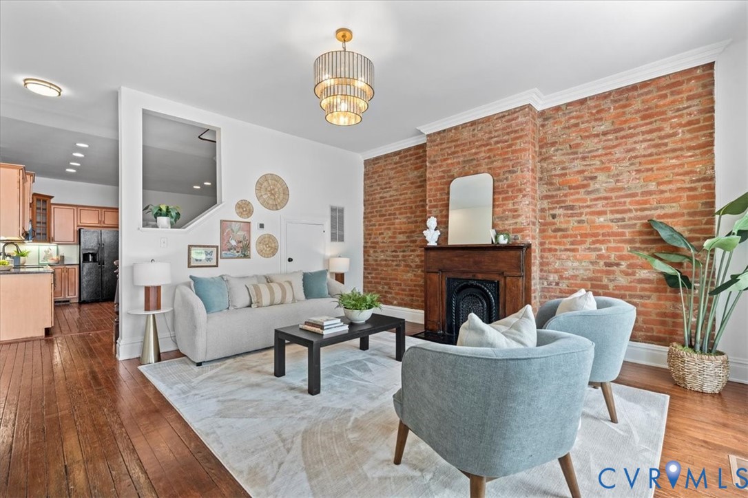 Exposed brick wall with a wood-mantel fireplace, hardwood flooring, and a tiered chandelier