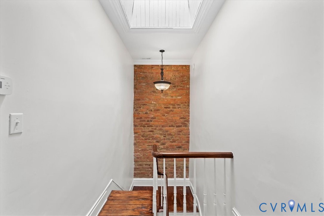 Exposed brick accent wall, wood-finish flooring, skylight, pendant light fixture, and white painted walls