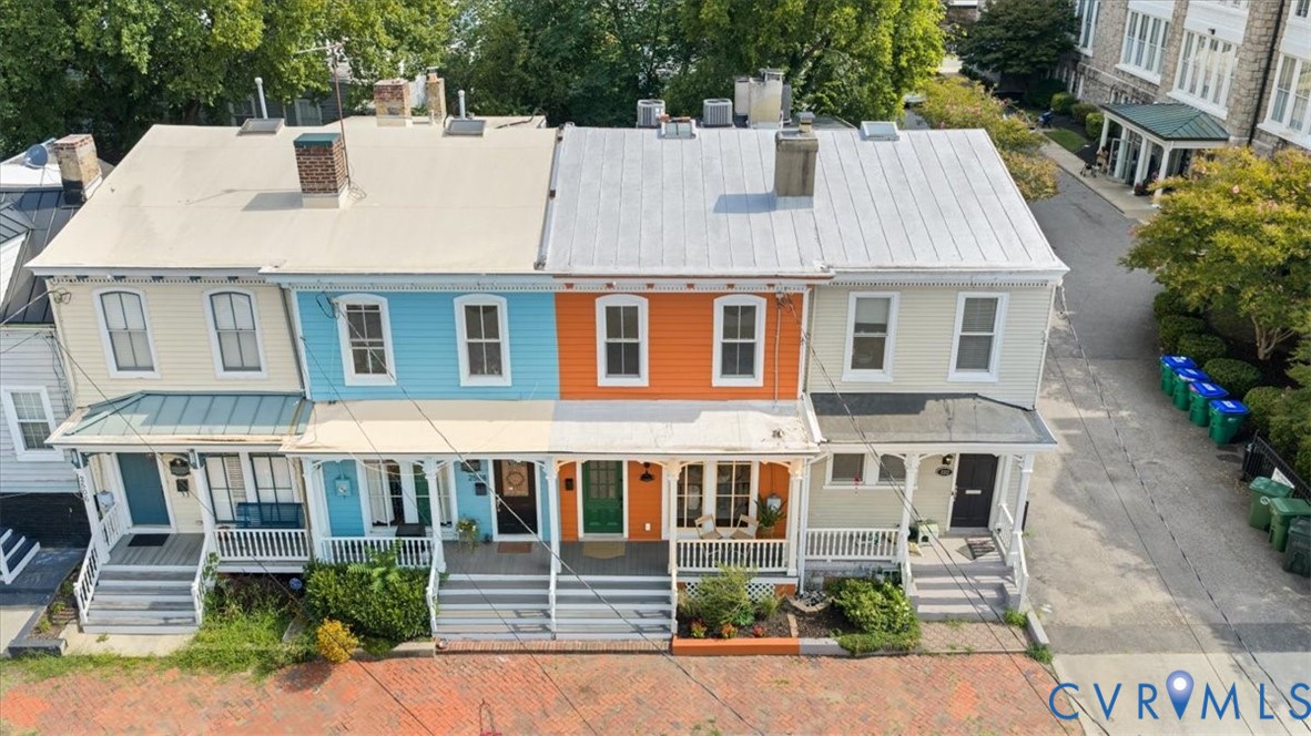 Colorful rowhouse facade with covered front porch, white railings, and brick walkway