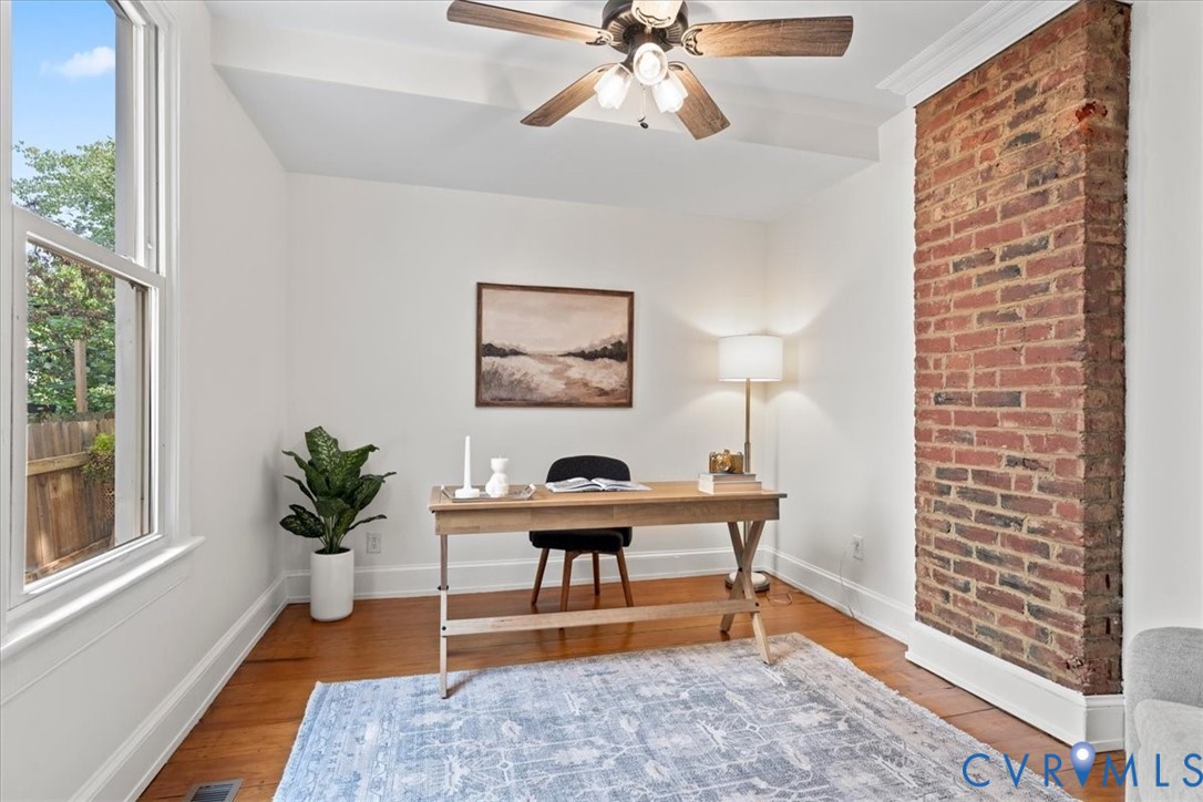 Hardwood flooring, exposed brick architectural feature, ceiling fan, white trim, and a large window