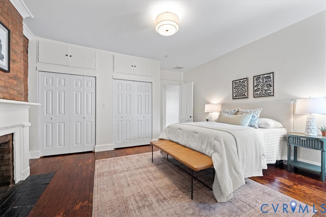 Exposed brick fireplace with a white mantel, wood-finish flooring, and white bi-fold closet doors with upper cabinetry