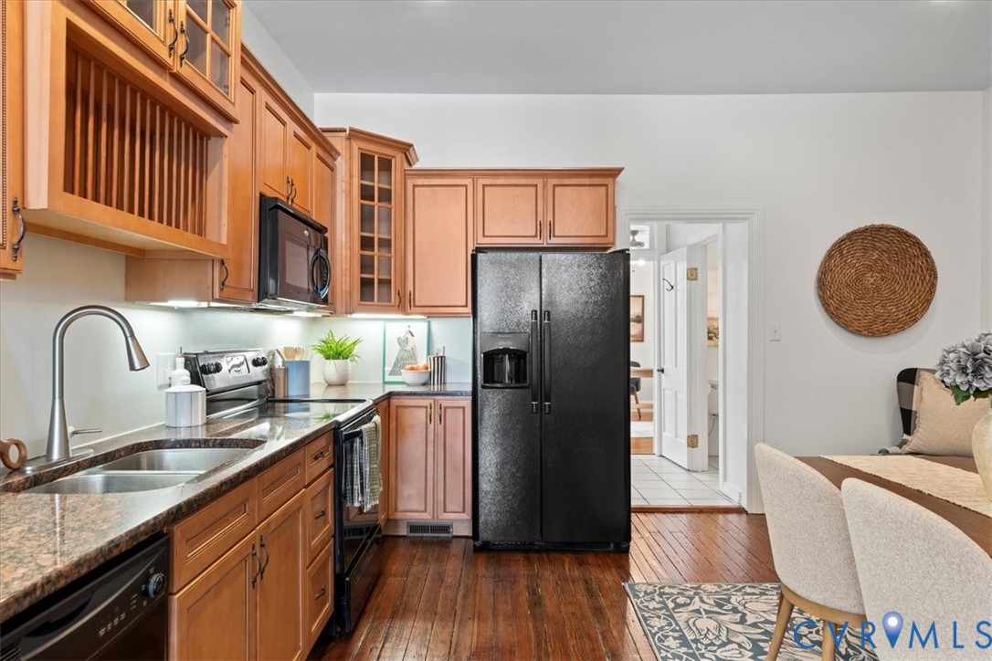 Wood-finish flooring, L-shaped counter, under-cabinet lighting, black appliances, and wooden cabinetry