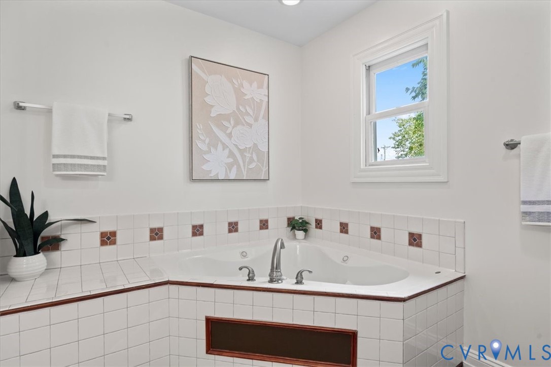 Corner soaking tub with a tiled surround, accent trim, and a double-hung window