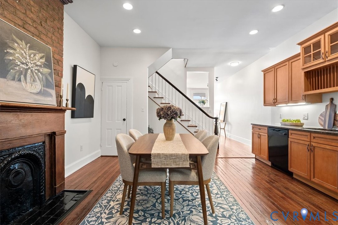 Hardwood flooring throughout, exposed brick accent wall, wood-mantel fireplace with cast iron insert, wood cabinetry with under-cabinet lighting, and recessed ceiling lighting