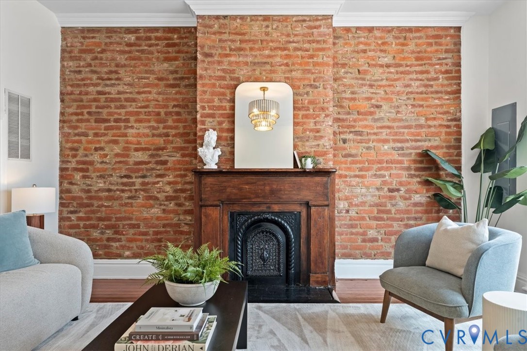 Exposed brick wall with crown molding, a wood-finish mantel, and a dark metal fireplace insert