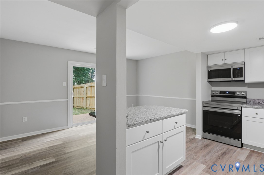 Contemporary kitchen featuring white cabinetry, stainless steel appliances, and a granite-finish island with storage
