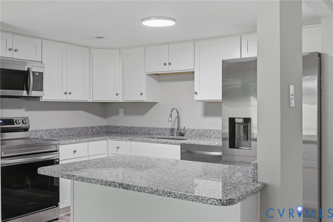 Modern kitchen featuring white cabinetry, speckled countertops, stainless steel appliances, and a built-in kitchen island